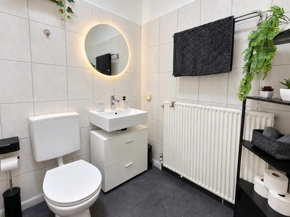 Badezimmer mit beleuchtetem Rundspiegel und hellen Fliesen