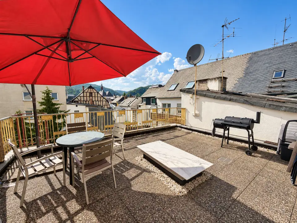 Gemeinsam genutzte Terrasse mit Sitzgruppe, rotem Sonnenschirm und Grill