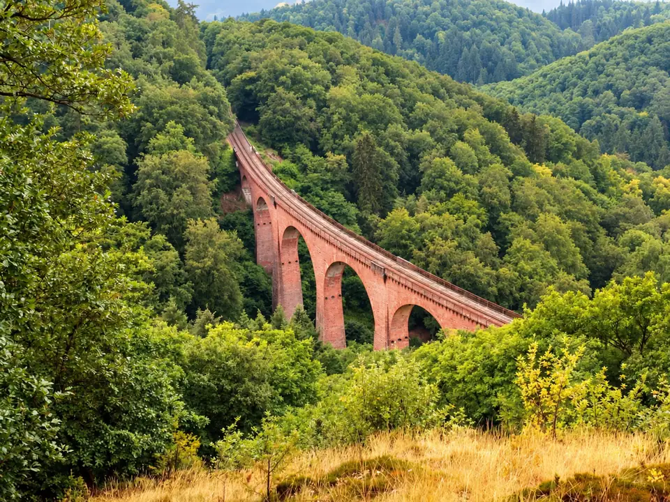 Roter Bahnviadukt in einem grünen bewaldeten Tal